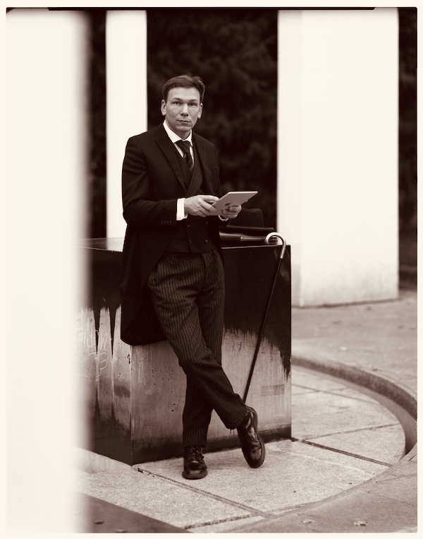 herr mika aka Mikael GB Horstmann im Stresemann-Anzug am Brunnen im Metzlerpark in Frankfurt am Main.